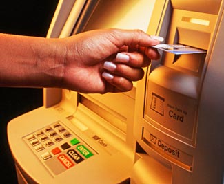 Egy bankautomata látható a képen, amint egy ember éppen belehelyezi a kártyáját