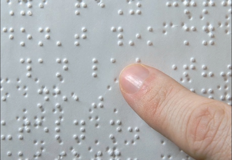A képen egy Braille-lap látható, amint valaki a kezével olvassa