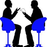 Két férfi fekete sziluettje, egyikük papírlapot tart kezében, közben beszélgetnek, a másik fél gesztikulál. Mindketten egy-egy erősen kontrasztos hatású kék forgószékben ülnek.​