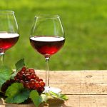 A képen két pohár vörösbor látható, egy fürt szőlővel, egy fából készült asztalon