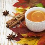 A képen egy bögre tea látható őszi faleveleken