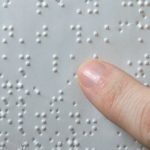 A képen egy Braille-írással készített papír látható, amit valaki az ujjával olvas