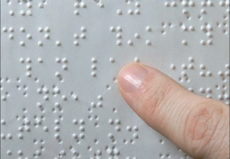 A képen egy Braille-írással készített papír látható, amit valaki az ujjával olvas