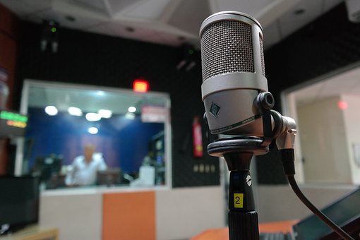 A fotó előterében mikrofon, a hátterében egy stúdió képe látható.