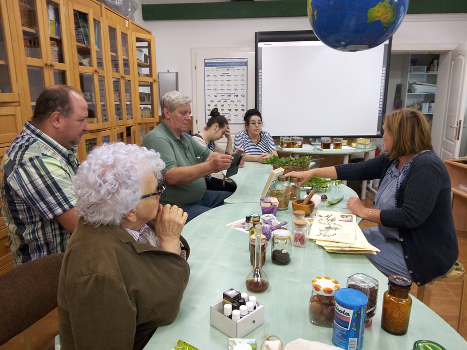 Az asztal körül a csoport tagjai és a múzeumpedagógus, az asztalon gyógy-és fűszernövények láthatók.