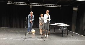Fehérbot nap, születésnap Zuglóban - Fodor Ágnes elnök köszönti a vendégeket, mögötte a két közösségi civilszervező és vakvezető kutyáik.