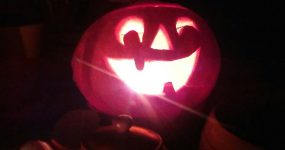 Őszbúcsúztató utó-utó-Halloween-buli jelmezversennyel - egy vigyorgó töklámpás a sötétben, előtte teáskanna teteje látszik.