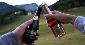 Két férfi keze látszik, mini pezsgős üvegekkel koccintanak.